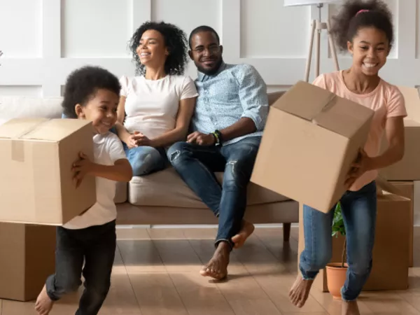 Parents sit on a couch while two children play with boxes of household goods ready to be shipped.