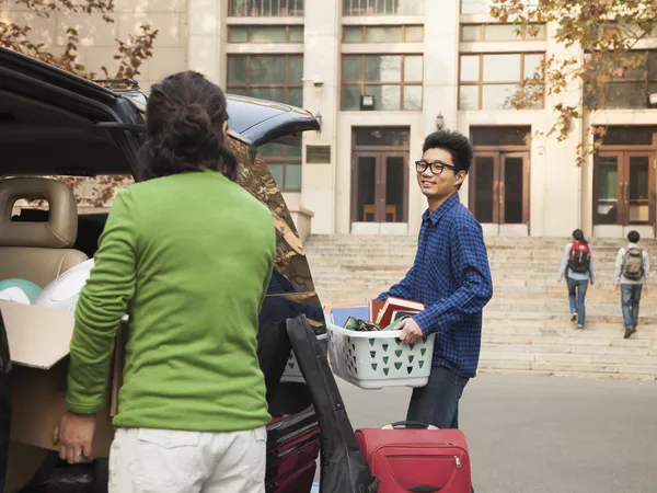 Male student and parent unloading the car at a dorm after moving to college across the country