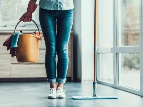 Woman with bucket of cleaning supplies, ready to clean with her apartment cleaning guide.