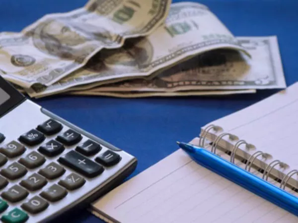 Person calculating moving costs with paper, pen, calculator and paper money.