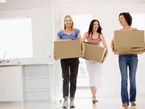 Three women carrying moving boxes, helping their friend move.