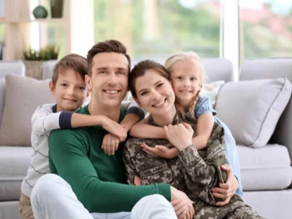 Mother, in military uniform, with father and two children, sitting in the floor hugging together.