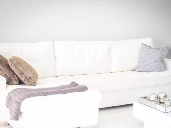 A white couch in a living room, ready to be wrapped for a move.