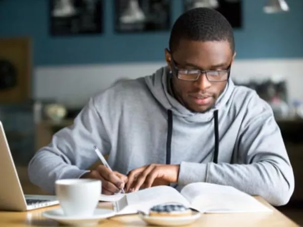 Male student deciding on the cheapest way to move to college with laptop, pen and paper.
