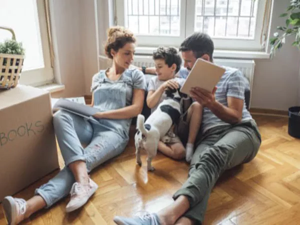 A mother, son, father and family dog sit on the floor while the parents discuss an upcoming move with their son.
