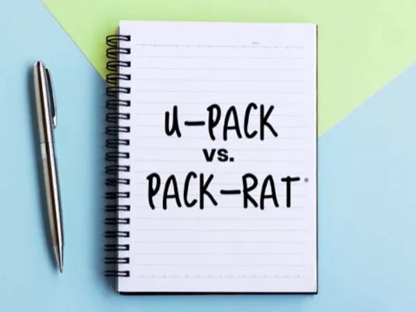 Notepad with "U-Pack vs. Pack-Rat" written on it next to a pen on a blue and green table.
