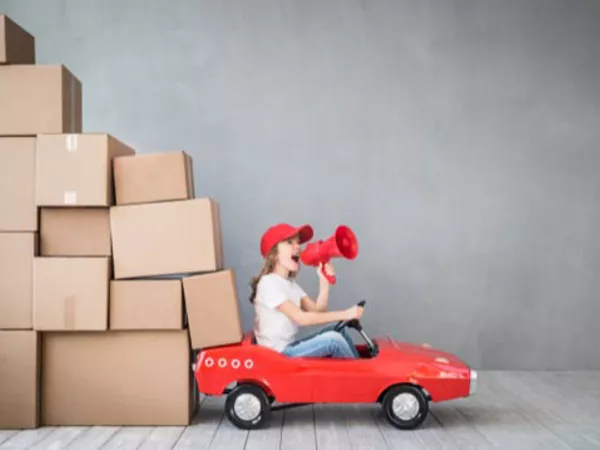 Young woman in a red toy car uses a megaphone to ask for help for her unique moving circumstances.