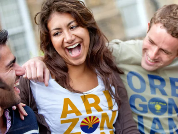 Group of people laughing while wearing shirts saying what people from Arizona and Oregon are called.