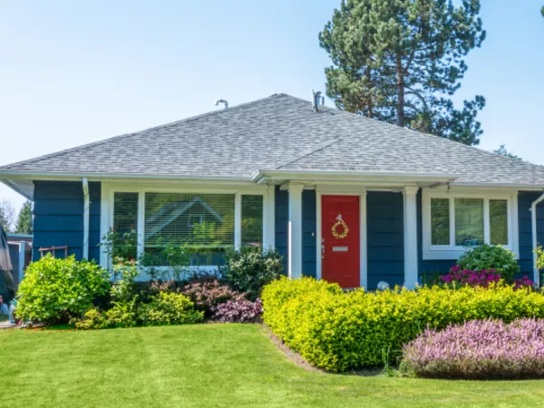 Blue house with a red front door and pretty landscaping.