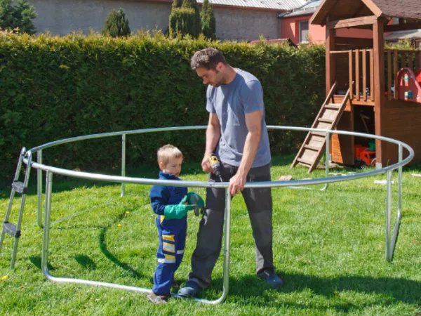 Father and son take apart a trampoline in a backyard.