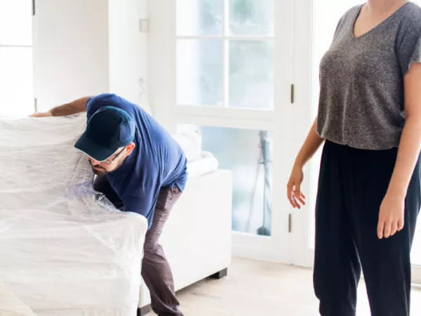 A woman watches as two movers pick a sofa she prepared for the moving crew.