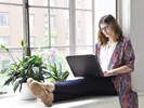 Woman sitting in a window seat, using her laptop to avoid Craiglist scams online.