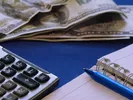 Person calculating moving costs with paper, pen, calculator and paper money.