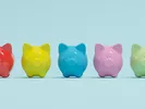 A line of brightly colored piggy banks sit side by side against a light blue background.