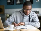 Male student deciding on the cheapest way to move to college with laptop, pen and paper.