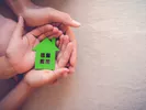 Family holding green paper house in their hands.