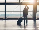Man waving goodbye to friends and family at the airport while pulling luggage.