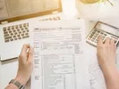 Hands holding an income tax return form and using a calculator to determine deductions.
