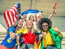 A crowd waves flags and air horns cheering on athletes at an Olympic venue.