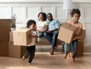 Mom and dad sitting on the couch while two children play with boxes of household goods ready to be shipped.