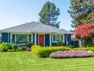 Blue house with a red front door and pretty landscaping.