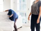 A woman watches two movers pick up her sofa