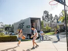 Children play basketball in a driveway while parents load a freight trailer for moving